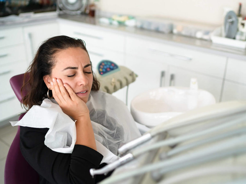 image of a woman sitting in a dental chair holding her cheek in pain