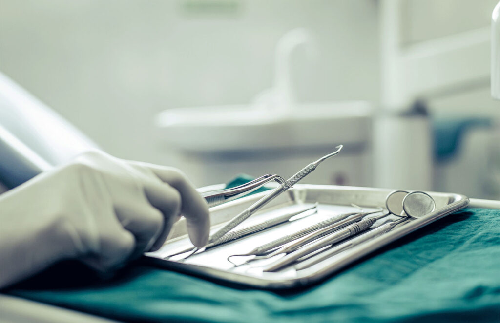 image of dental tools on a tray with a hand grabbing one of the tools